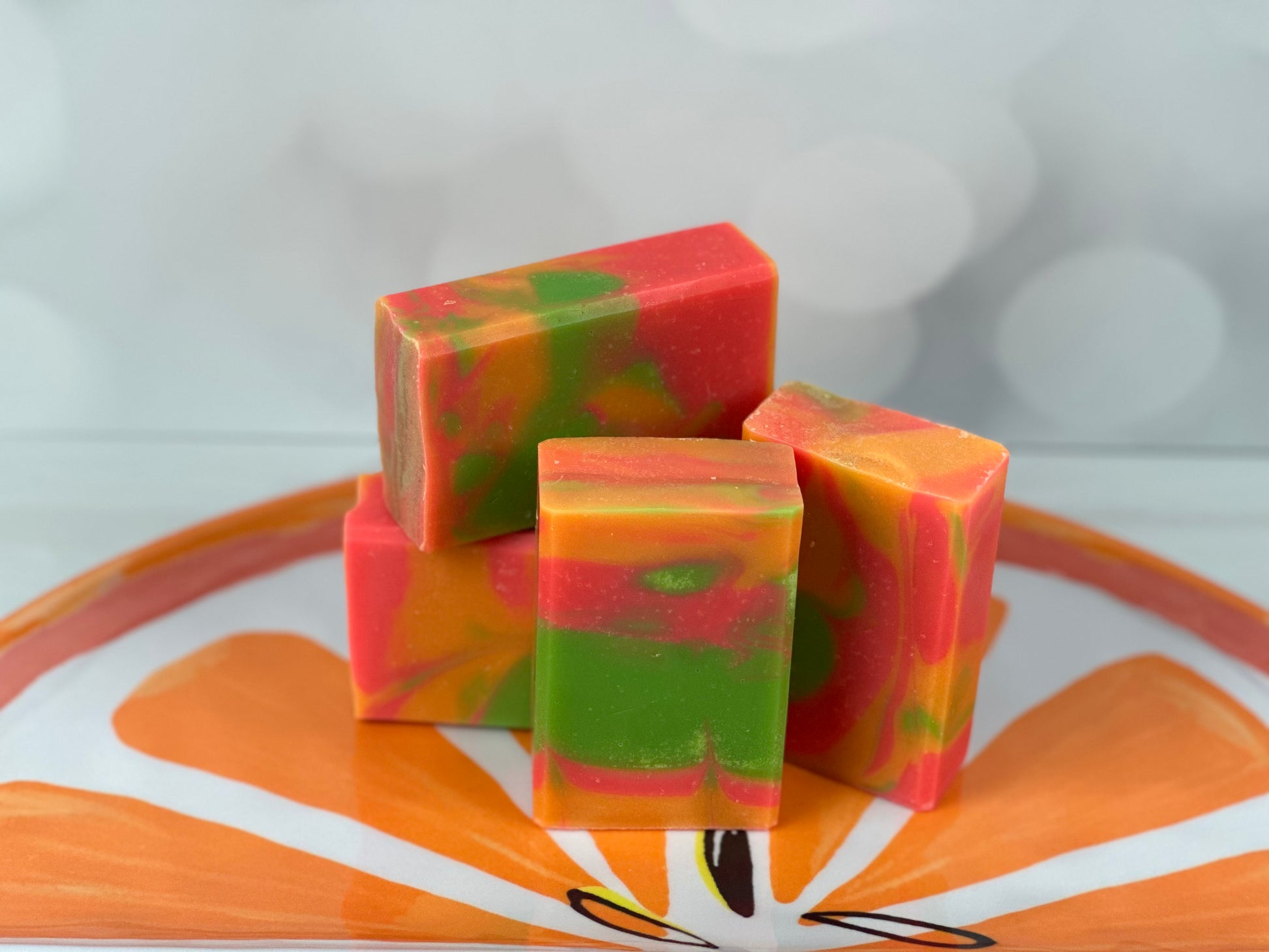 Bright orange, pink and lime green bars of soap sitting on a tray with an orange slice design