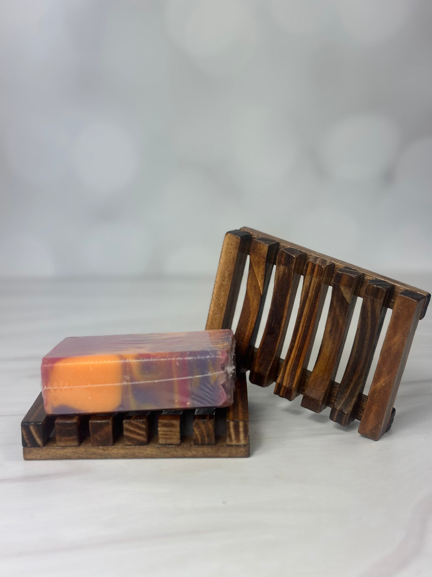 Wooden slotted soap tray with a bar of purple orange and pink sitting on it to show how it’s used 