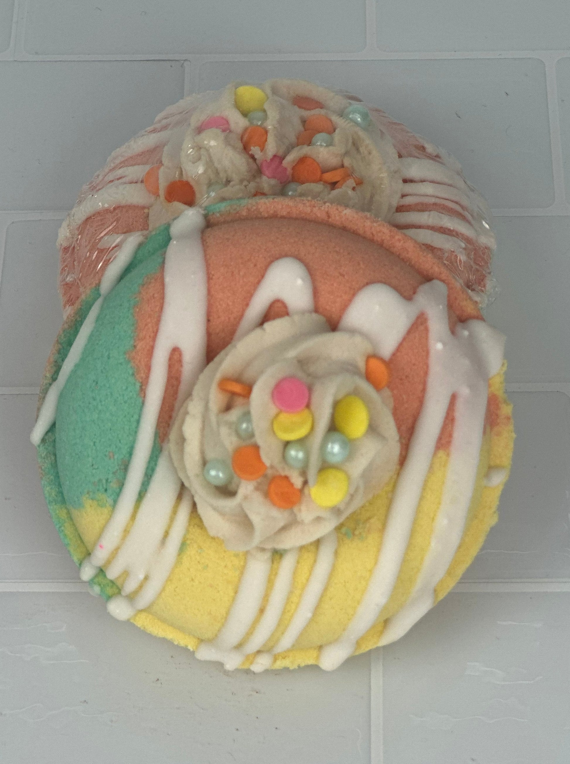 Donut shaped bath bomb with white frosting and sprinkles, colored in yellow mint green and coral