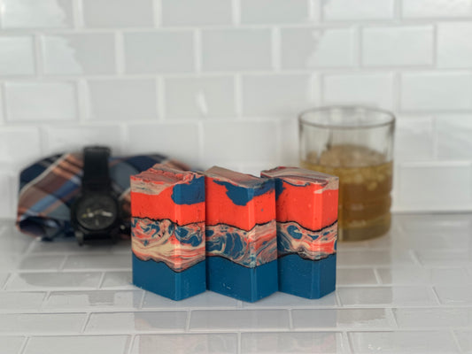 Orange blue and white bars of soap with cocktail glass, mens tie and watch in the background on white tile