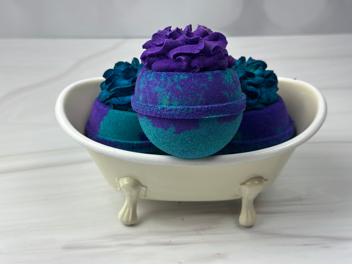3 purple and turquoise round bath bombs sitting in a small white bath tub
